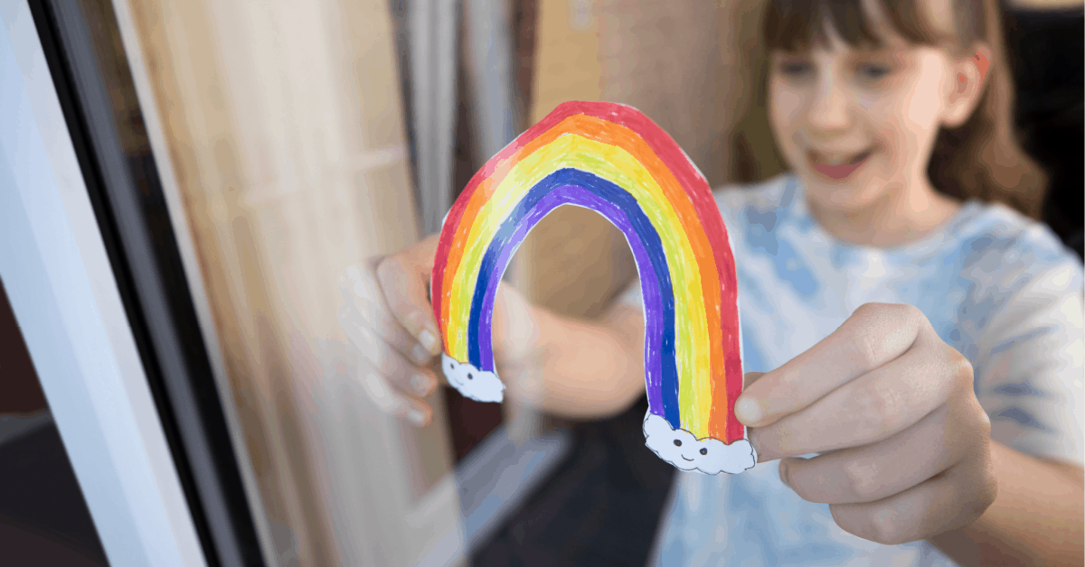 Photo of young girl hanging up homeschool rainbow artwork in kitchen window.