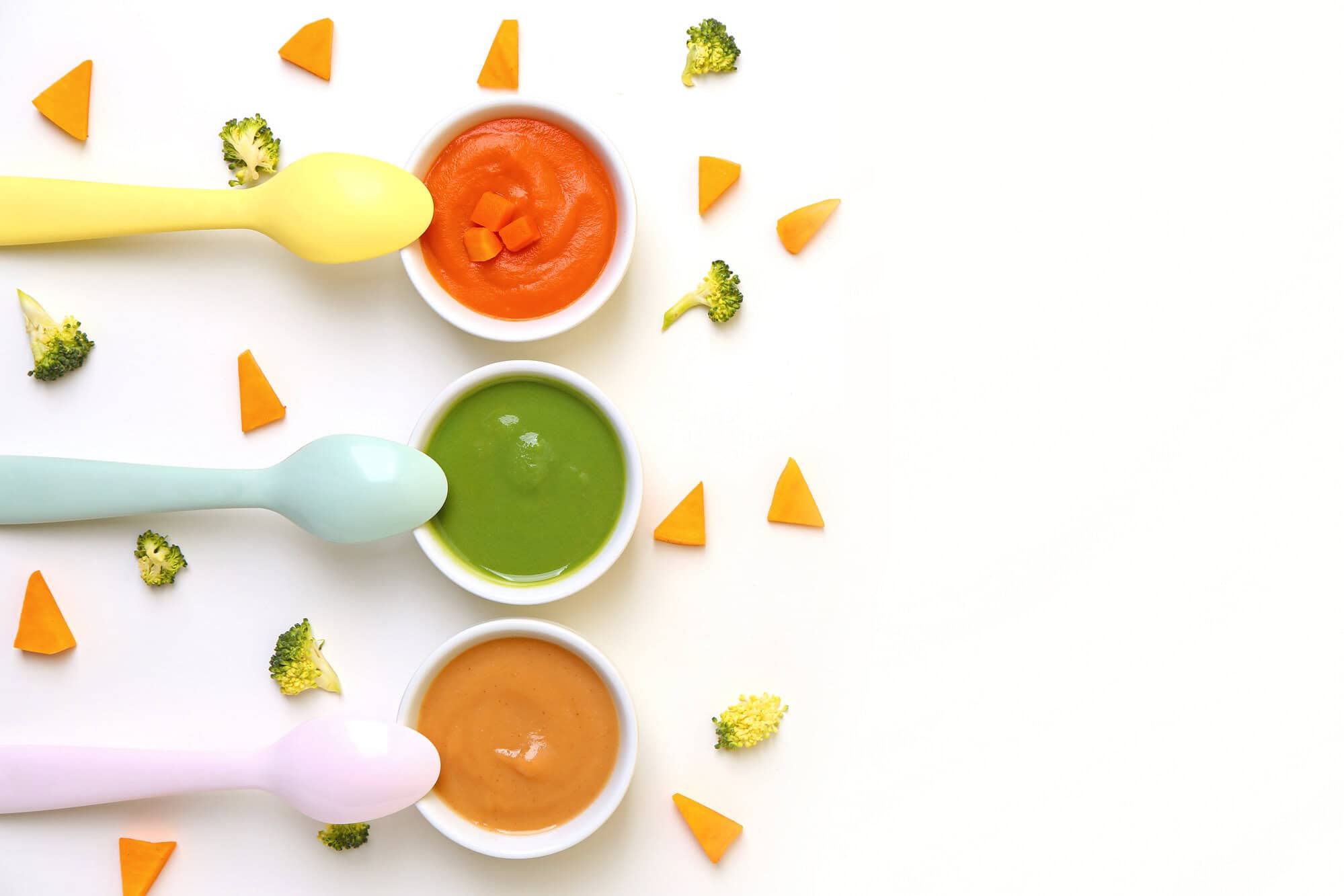 Composition with bowls of healthy baby puree and cut vegetables on white background