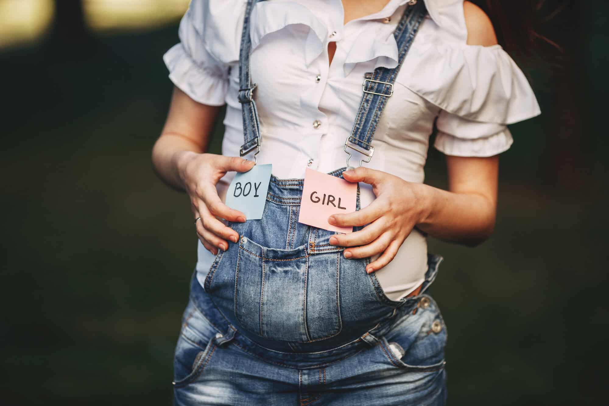 Pregnant woman's hands with BOY and GIRL cards near belly. Intrauterine growth, pregnancy, maternity, unborn baby gender