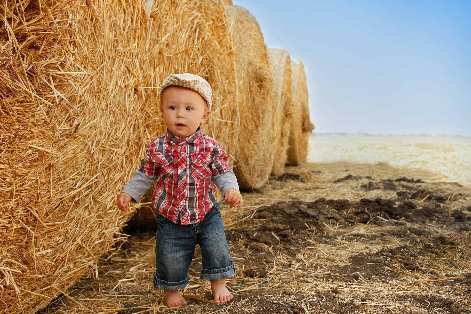 little boy playing in a cowboy hat on bales of hay