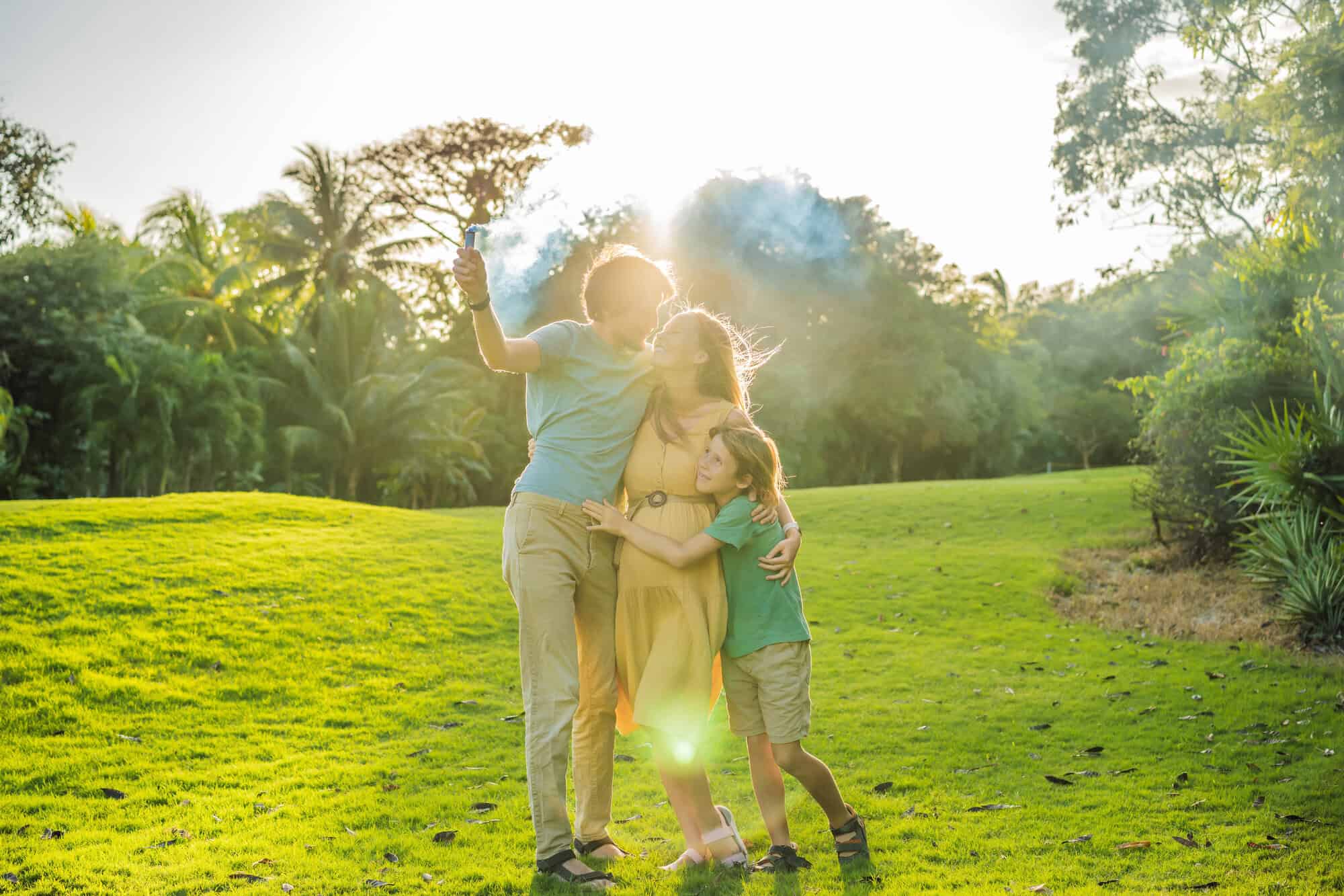 Pregnant mom, dad and son at the gender party on the golf course release blue smoke. Gender reveal announcement on the golf course. Loving family expecting baby boy. Happy moments.
