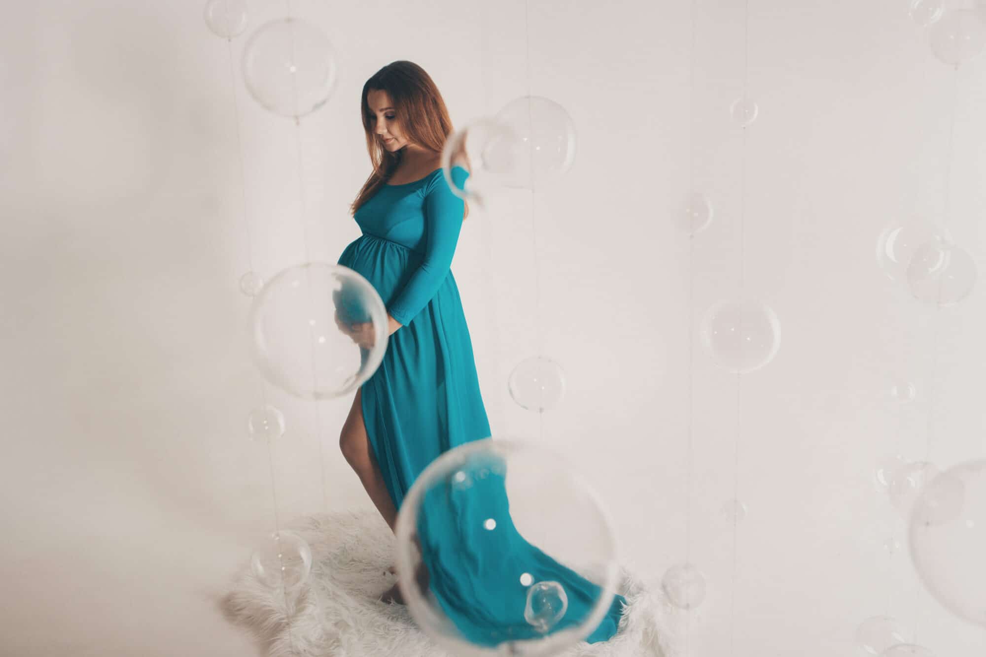 Isolated photo on a white background: a beautiful pregnant woman in a blue dress put her hands on her stomach