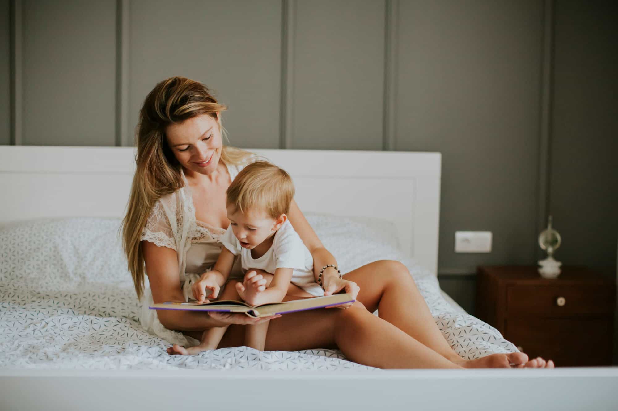 Mother and little boy reading book in bed at home