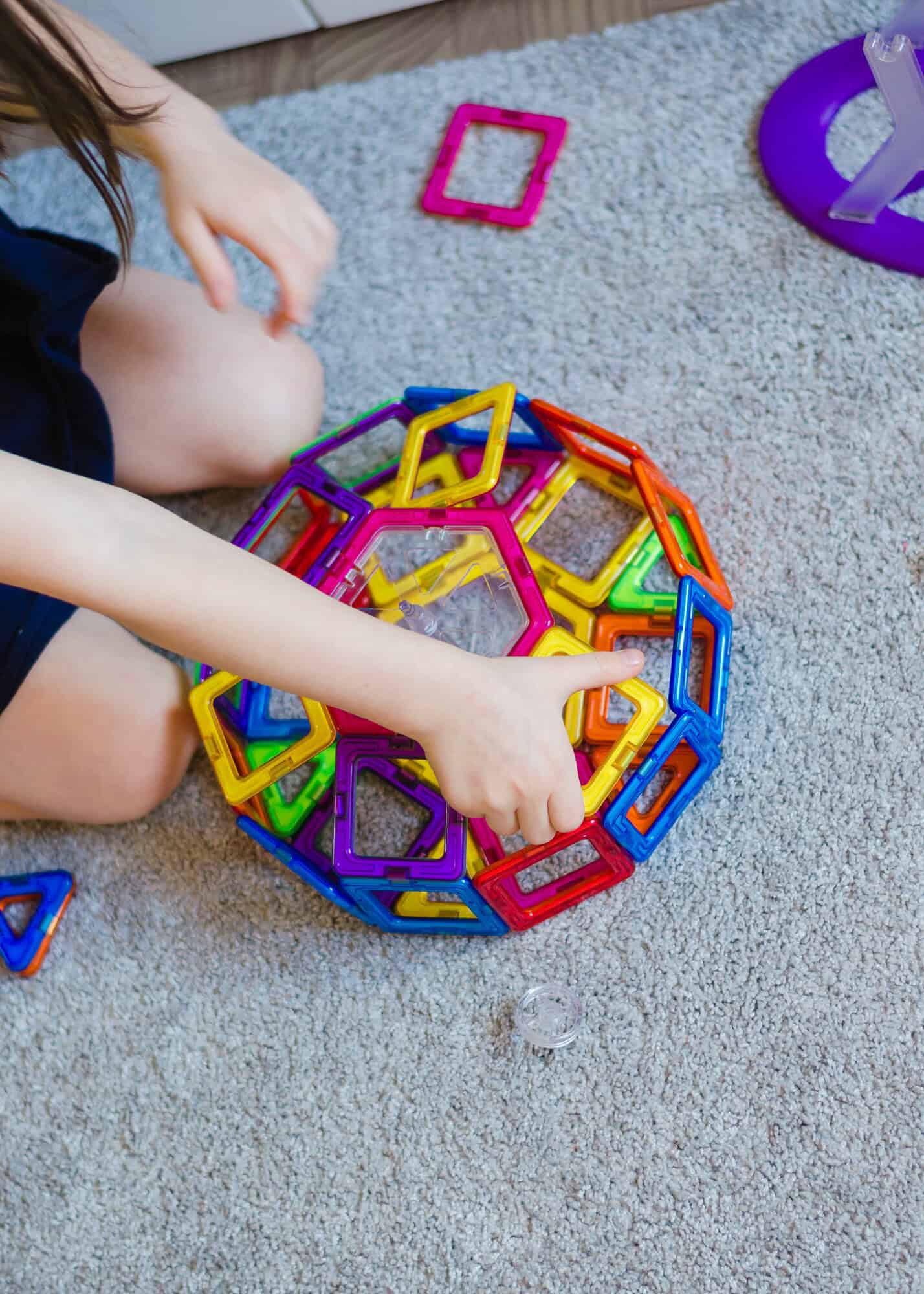 Kid plays with a magnetic constructor toy. A little child girl is playing with colorful blocks. Close up. Girl playing intellectual toys. Children's magnetic designer for development of motor skills.