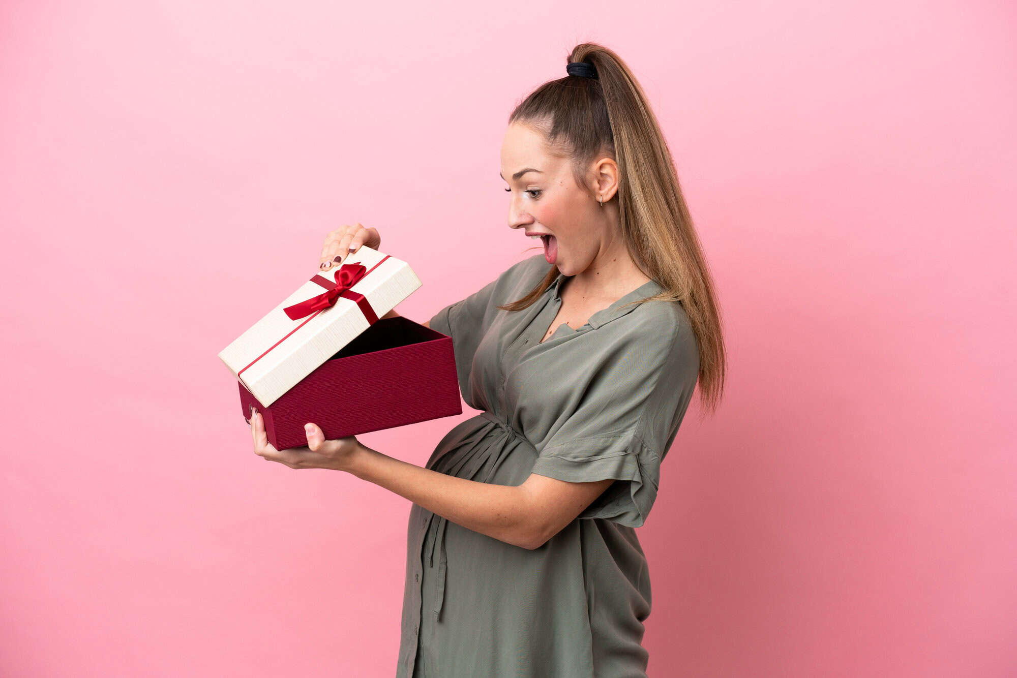 Young woman isolated on pink background pregnant and holding a gift with surprised expression