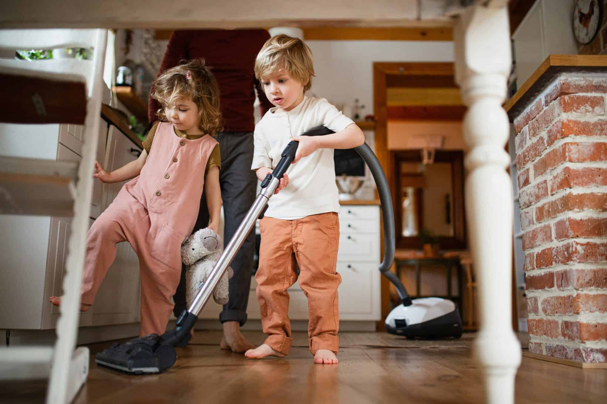 Two little kids practice independence by helping their dad vacuum the house.