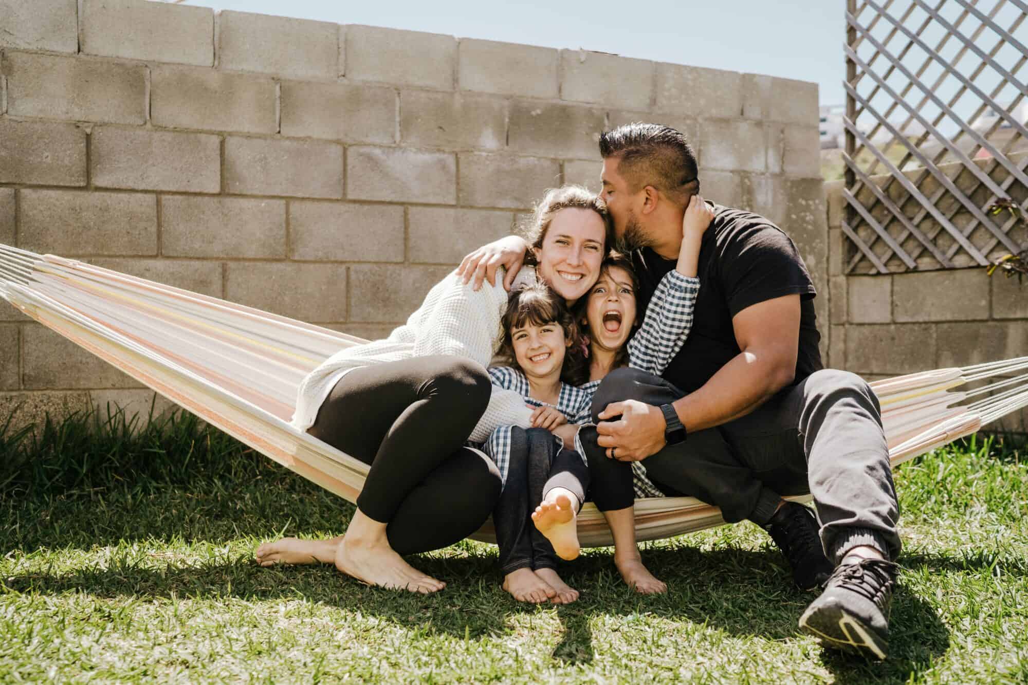 Mom and dad sit in hammock outside with their two kids.