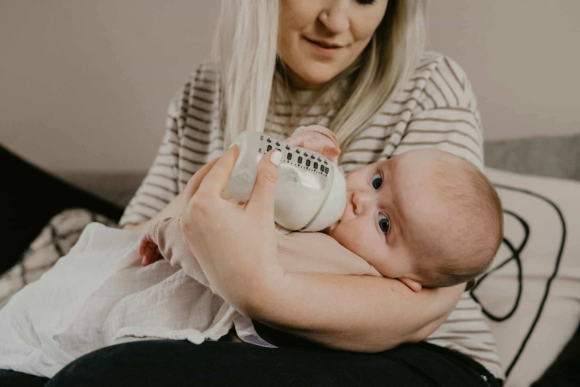 Mom feeding bottle to new baby while sitting on a couch.