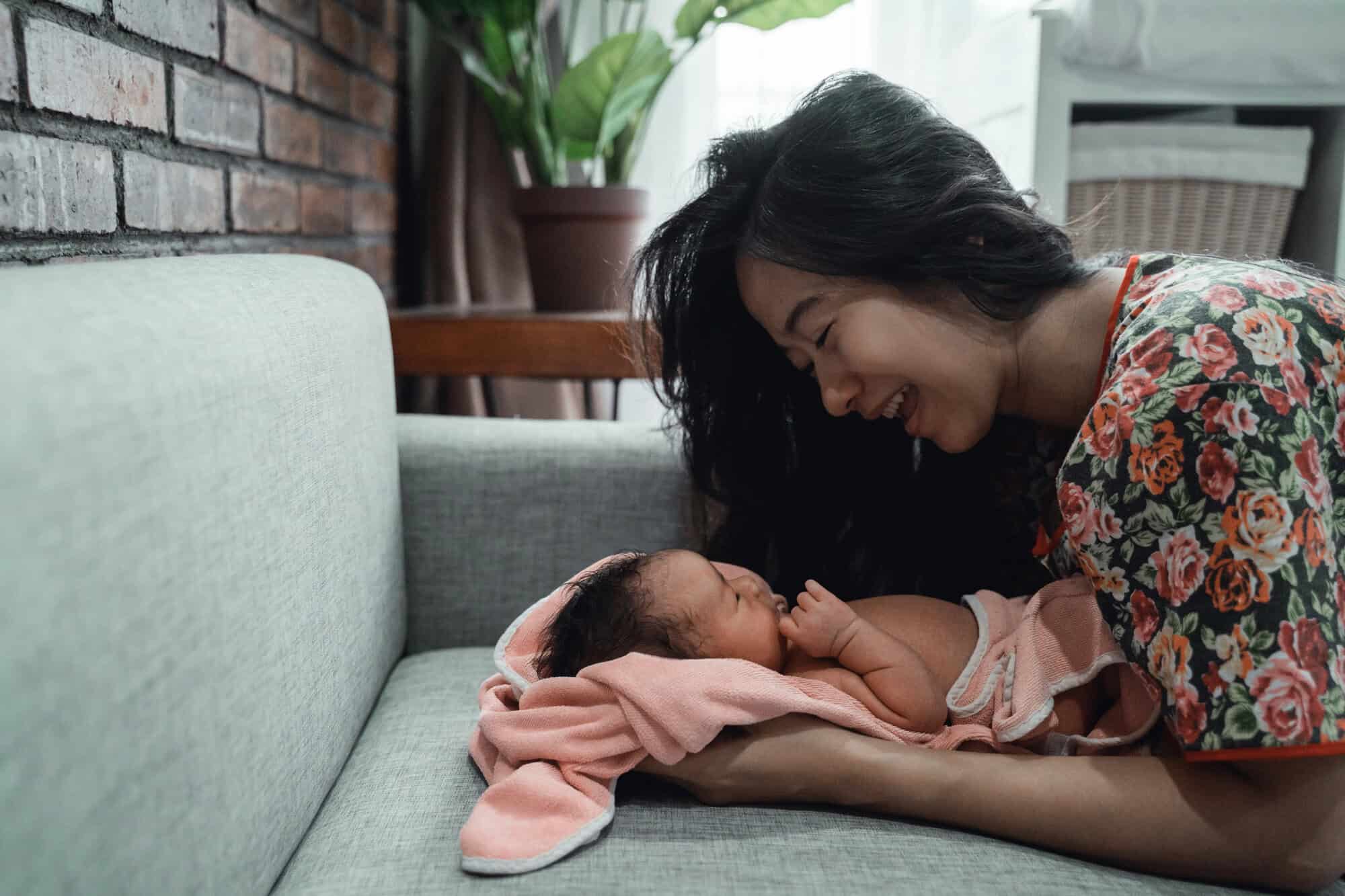 Smiling mom cuddling her newborn baby on the couch.